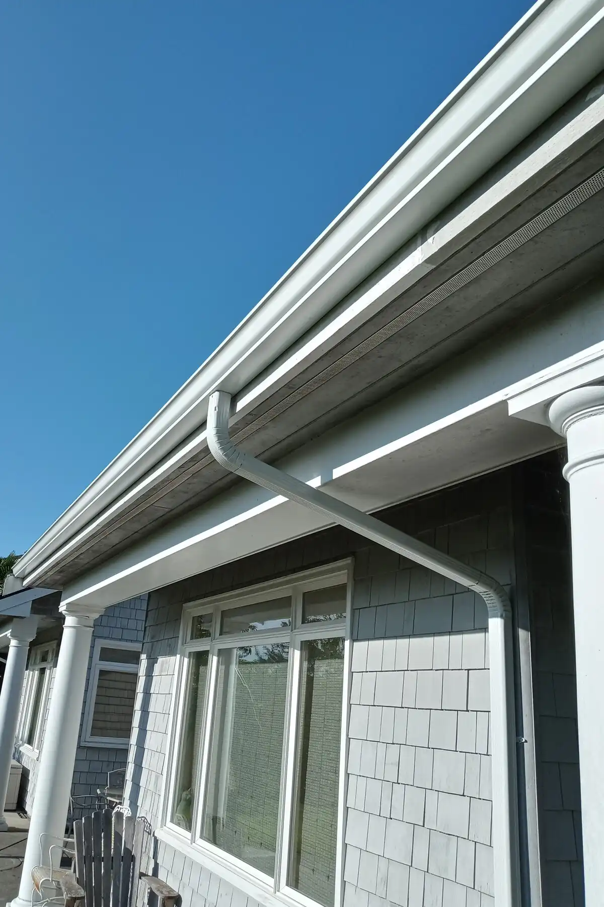 A white 5k gutter and downspout on a blue house with shake siding.