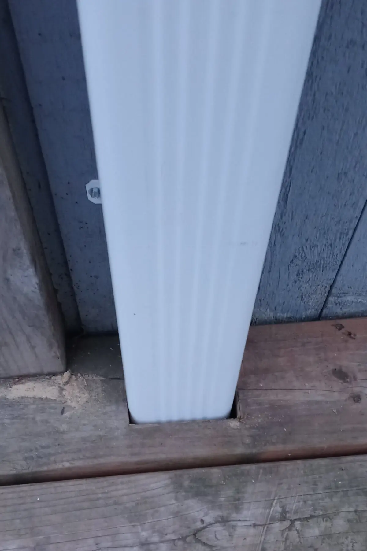 A white downspout passing through a custom cut hole in a wooden deck.